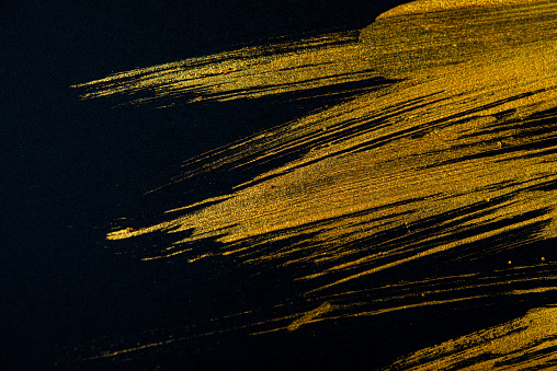 Golden strokes of acrylic paint with an art brush on a black background. Abstract background. Web banner.
