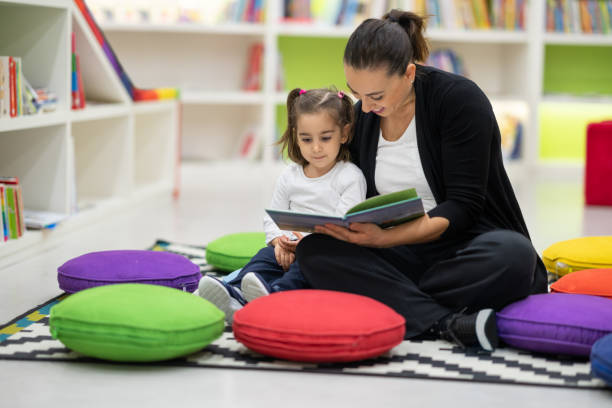 母と娘は保育園で本を読んでいます - child reading mother book ストックフォトと画像