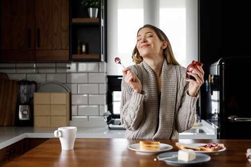 Portrait of happy young woman eating jam in the kitchen