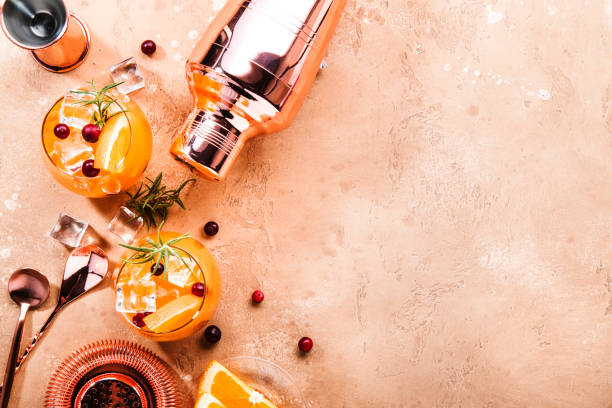 Orange Cranberry Rosemary and Vodka cocktail, copper bar tools, beige background, hard light, top view Orange Cranberry Rosemary and Vodka cocktail, copper bar tools, beige background, hard light, top view non alcoholic beverage photos stock pictures, royalty-free photos & images
