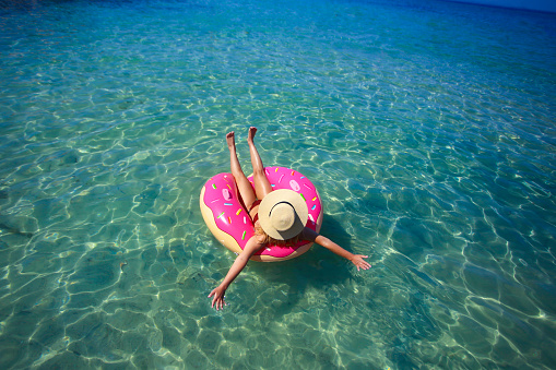 Young woman enjoying the beach during the summer vacation, floating on an inflatable donut ring. About 25 years old, Caucasian blonde.