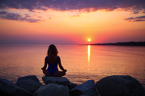 Young woman doing yoga on the beach during a sunset. Silhouette of an unrecognizable female.