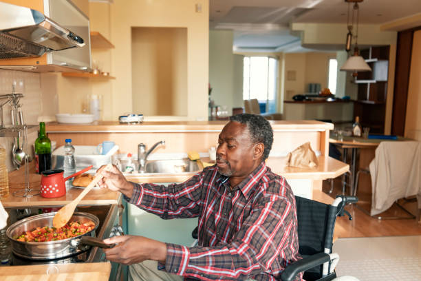 Senior Afro-American in Wheelchairs is Preparing a Lunch at Home Disabled Afro-American Person is Enjoying in Preparation of Delicious Lunch. A Senior African is Cooking a Dinner in Domestic Kitchen. accessibility for persons with disabilities stock pictures, royalty-free photos & images