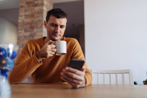 istock Man drinking coffee at home and using smartphone 1203138869