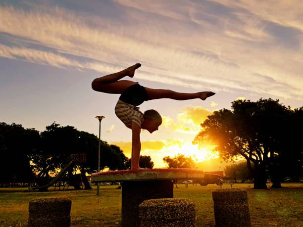 A young female gymnast is seen in silhouette as she performs an acrobatic handstand outdoors at sunset.