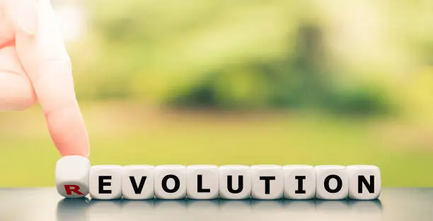 Photo of Evolution instead of revolution. Hand turns a dice and changes the word 