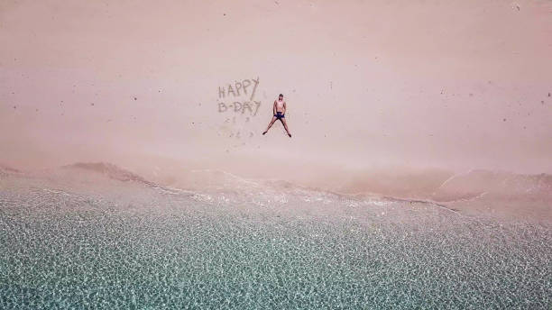 maumere - un colpo di drone di un uomo sdraiato su una spiaggia accanto al cartello 'buon compleanno' - flores man foto e immagini stock