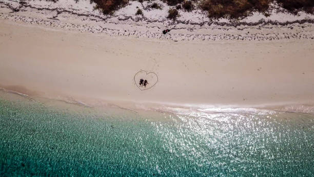maumere - un drone sparato da una coppia seduta su una spiaggia in un cuore disegnato sulla sabbia - flores man foto e immagini stock