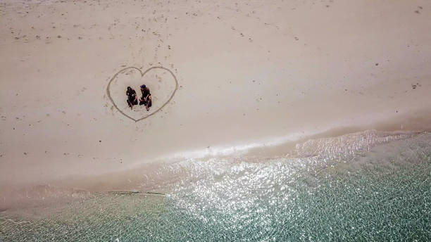 maumere - un drone sparato da una coppia seduta su una spiaggia in un cuore disegnato sulla sabbia - flores man foto e immagini stock