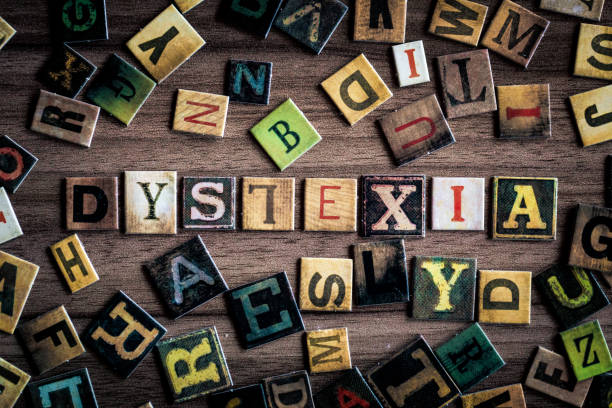 Color image depicting an overhead view of colorful letter tiles spelling out the word Dyslexia, with the 'L' upside down. The word is surrounded by a large collection of other alphabet letter tiles, in a haphazard arrangement.