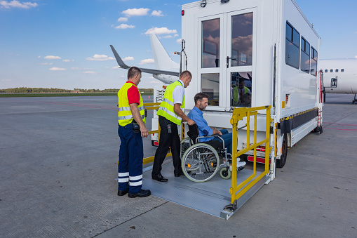 Modern elevator for disabled passenger standing next to the aircraft at the airport. Ground service men helping wheelchair passenger.