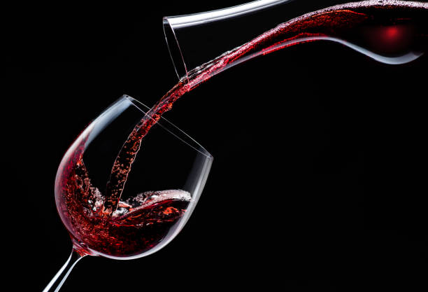 istock Red wine is poured into a wine glass on a black background. 1203163859