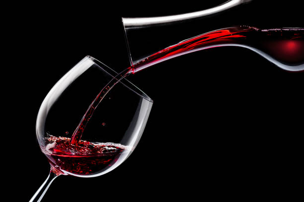 istock Red wine is poured into a wine glass on a black background. 1203164488