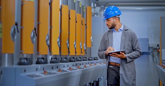 Male engineer using digital tablet while examining manufacturing machinery in factory.