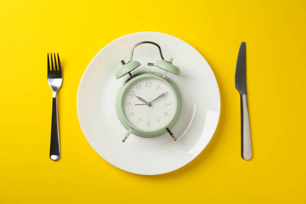 istock Plate with alarm clock, fork and knife on yellow background, top view 1203166426