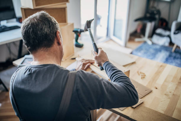 One senior carpenter in work suit using hammer to make wooden drawer