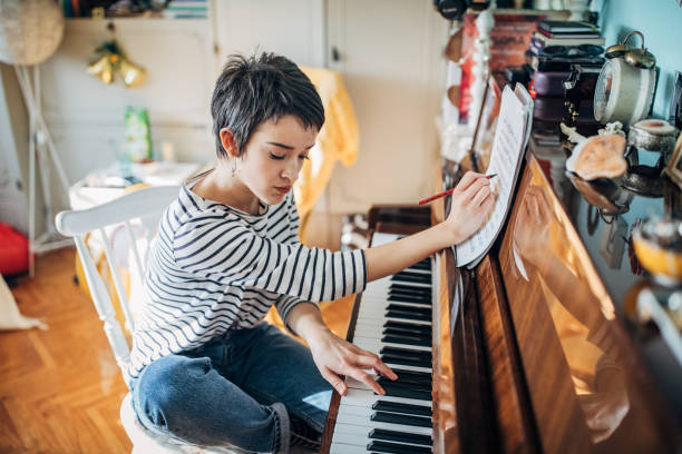 Young woman pianist composing music in her room at home One woman, young woman pianist playing piano and writing musical notes in her room at home alone. composer photos stock pictures, royalty-free photos & images