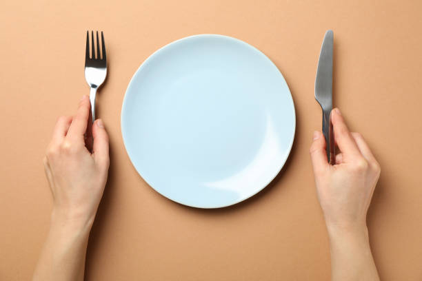 istock Female hands hold fork and knife on craft background with plate, top view 1203167649