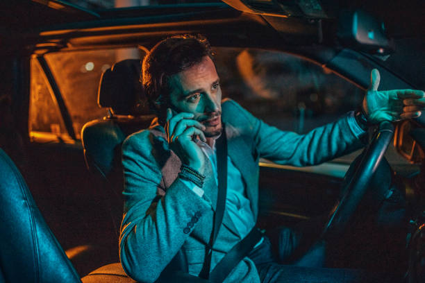 istock Gentleman driving a car talking on mobile in city at night 1203168155