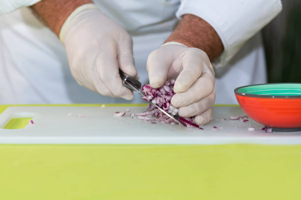 Male chef picks up freshly cut red onion dice from a cutting board with a knife. Cooking concept.