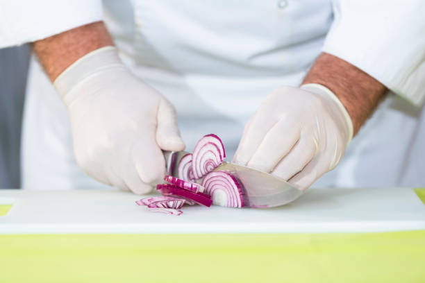 male chef with gloves cutting a delicious looking fresh red onion into slices on a cutting board. Cooking concept.