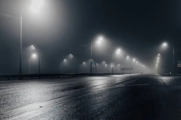 Photo of Foggy misty night road illuminated by street lights