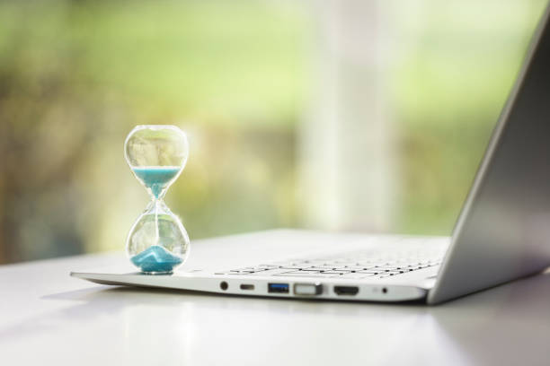 concetto di clessidra su computer portatile per la gestione del tempo - waiting wasting time time business foto e immagini stock