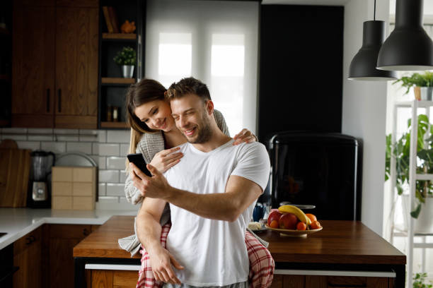 istock Young affectionate couple looking at mobile phone in the kitchen 1203174009