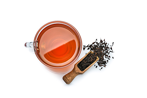 Black tea cup shot from above on white background. A wooden serving scoop with dried black tea leaves is beside the tea cup. High resolution 42Mp studio digital capture taken with Sony A7rii and Sony FE 90mm f2.8 macro G OSS lens