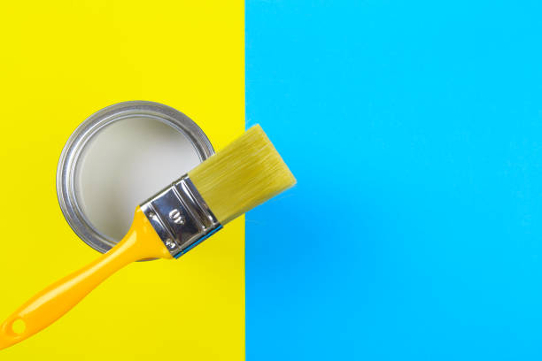 istock White Paint Can with Brush Top View On Yellow and blue  Background. 1203176071
