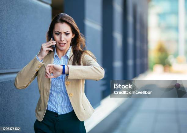 Schockierte Junge Geschäftsfrau Überprüft Zeit Auf Armbanduhr Während Handy Sprechen Stockfoto und mehr Bilder von Dringlichkeit
