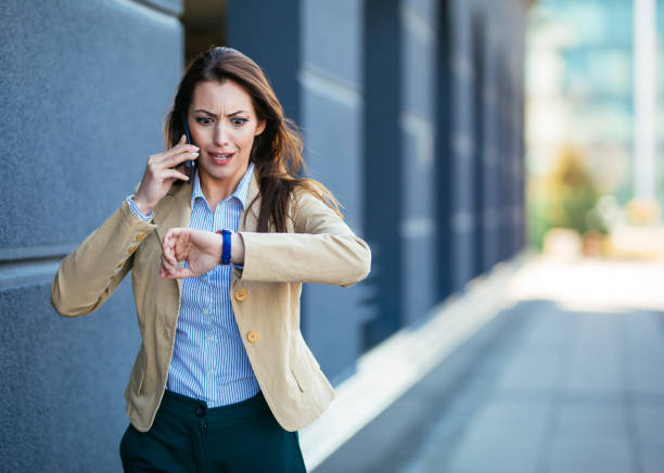 giovane imprenditrice scioccata che controlla il tempo sull'orologio da polso mentre parla cellulare - time pressure foto e immagini stock