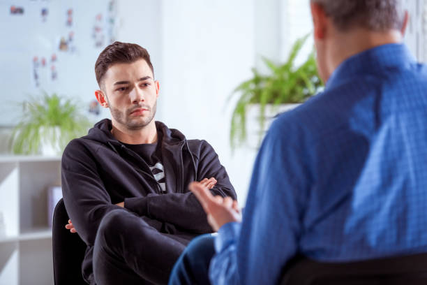 Serious university student listening to therapist Serious student listening to therapist. Mature professional advising young man during session. They are sitting in meeting at lecture hall. low self esteem stock pictures, royalty-free photos & images