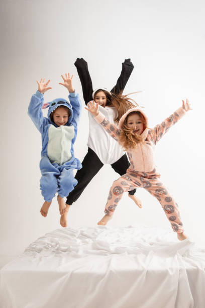 Children in soft warm pajamas having party colored bright playing at home Children in soft warm pajamas colored bright playing at home. Little girls having fun, party, laughting, jumping together, look stylish and happy. Concept of childhood, leisure activity, happiness. pyjamas stock pictures, royalty-free photos & images