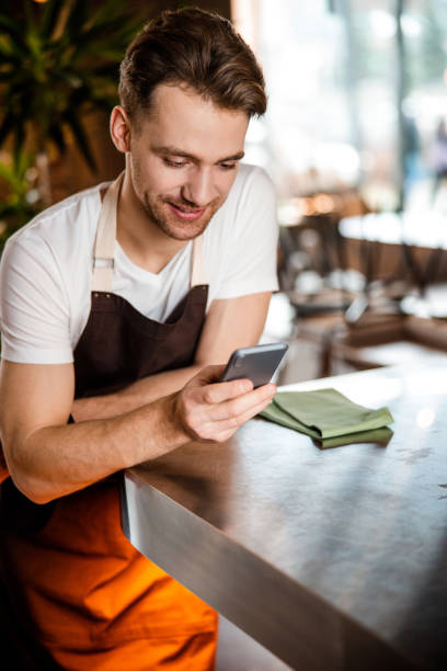 istock Attractive Caucasian waiter using his cellphone in romantic cafe 1203179752