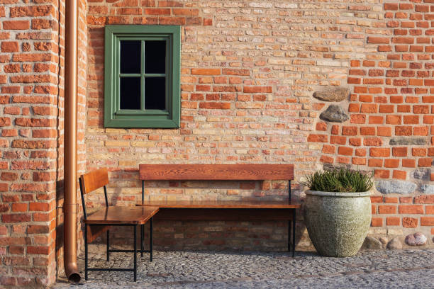 istock Empty bench in brick wall corner with small window. Vintage styles photography. Place inviting on rest. 1203179780
