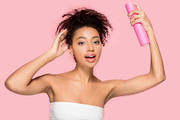 привлекательная афро-американская девушка с бутылкой лака для волос, изолированные на розовый - hairspray стоковые фото и изображения