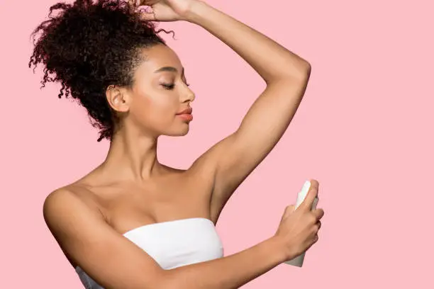 beautiful african american girl using spray deodorant, isolated on pink