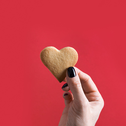 Homemade heart shaped cookies for Valentine's Day in female hand on red. Minimal. Concept.