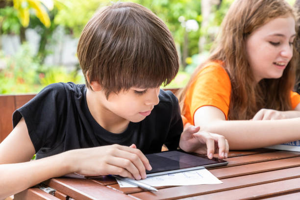 istock Cute boy using tablet while doing homework with his sister in garden at home 1203186006