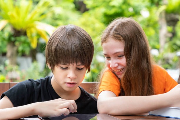 istock Cute boy using tablet while doing homework with his sister in garden at home 1203186016