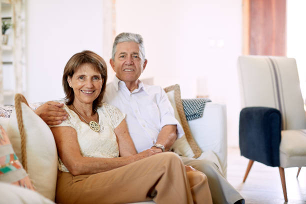 istock Senior couple sitting in the sofa with hand on shoulder and looking at the camera. 1203187511