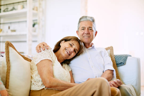 istock Senior couple sitting in the sofa embracing and looking at camera. 1203187527