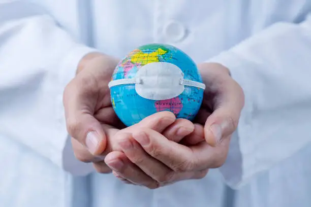 closeup of a caucasian doctor man holding a world globe with a protective mask placed over China, depicting the recent coronavirus outbreak