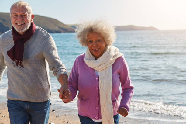 istock Active Senior Couple Running Along Winter Beach By Waves Holding Hands 1203187749