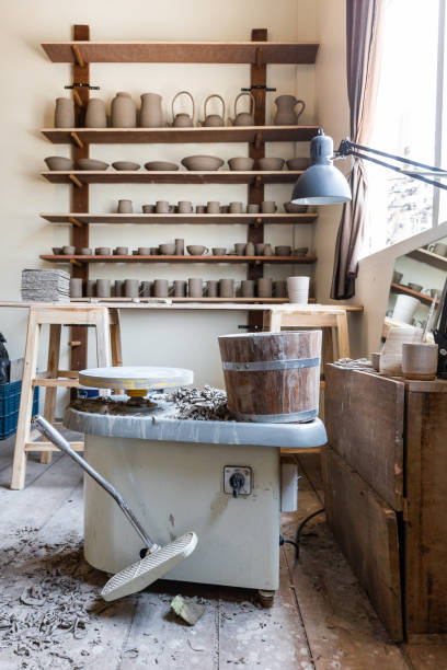 istock Wooden display shelf for hand crafted Ceramic such as bowls, plates and cups with Pottery Wheel Machine in foreground. Creative workshop. 1203187921