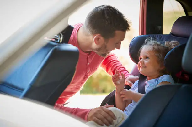 Father Securing Daughter Into Rear Child Seat Before Car Journey