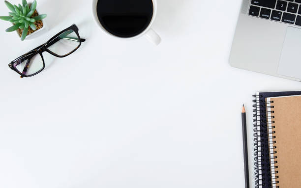 istock Flat lay, White office desk table with laptop, notebooks, pencil, black coffee cup and eyeglasses. Top view with copy space. 1203188081