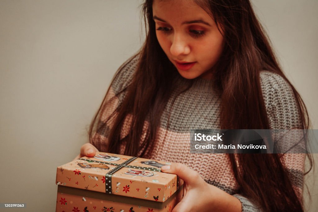 Teenage girl holding Christmas gift Teenage girl in grey-pink sweater holding Christmas gift against grey wall Beautiful People Stock Photo