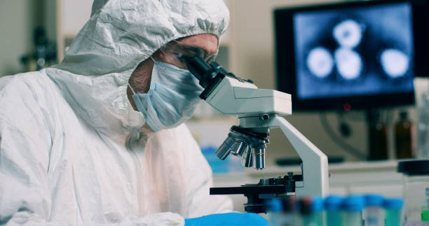 A research scientist working in his laboratory with a sample or specimen and an image of the Wuhan Coronavirus displayed on a computer screen.